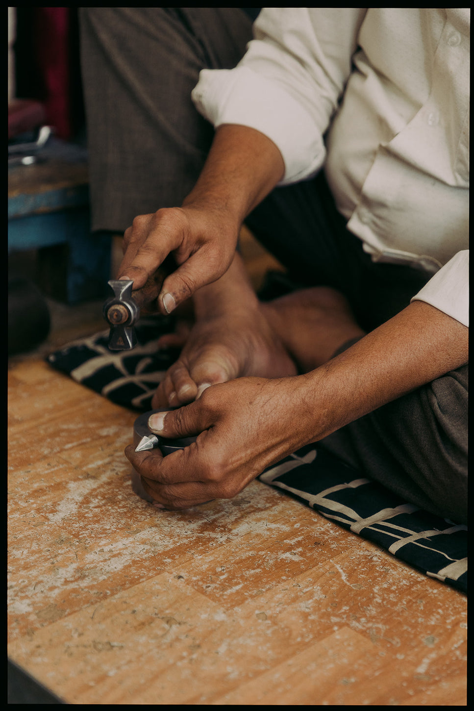 Gros plan sur des mains d’artisan façonnant un bijou à l’aide d’un outil, sur un sol en bois, illustrant le travail artisanal.