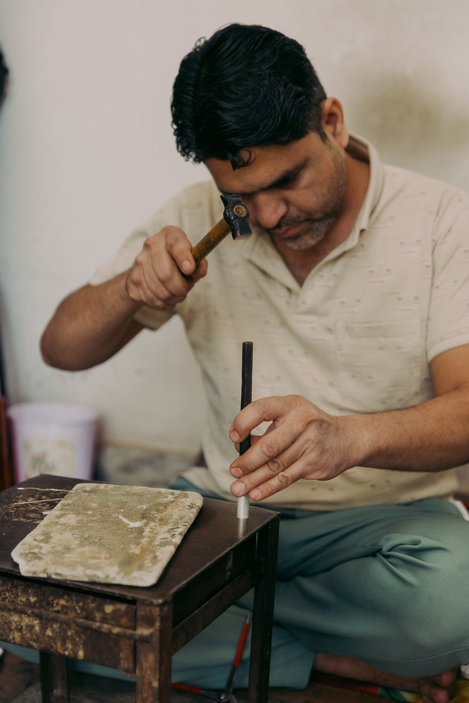 A craftsman sits at a workbench hammering a metal rod, focusing on shaping a jewelry piece with precision and traditional tools.