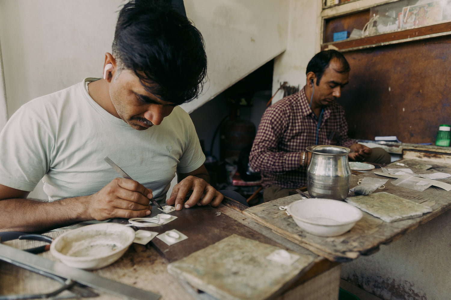 Two artisans carefully crafting jewelry at a wooden workbench, using precision tools and traditional techniques in a workshop setting.