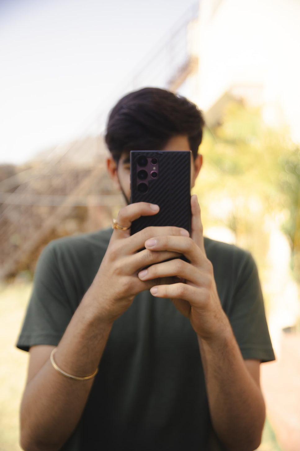 Young man holding a smartphone with a quad-camera setup, focusing on taking a photo outdoors, highlighting smartphone photography use.