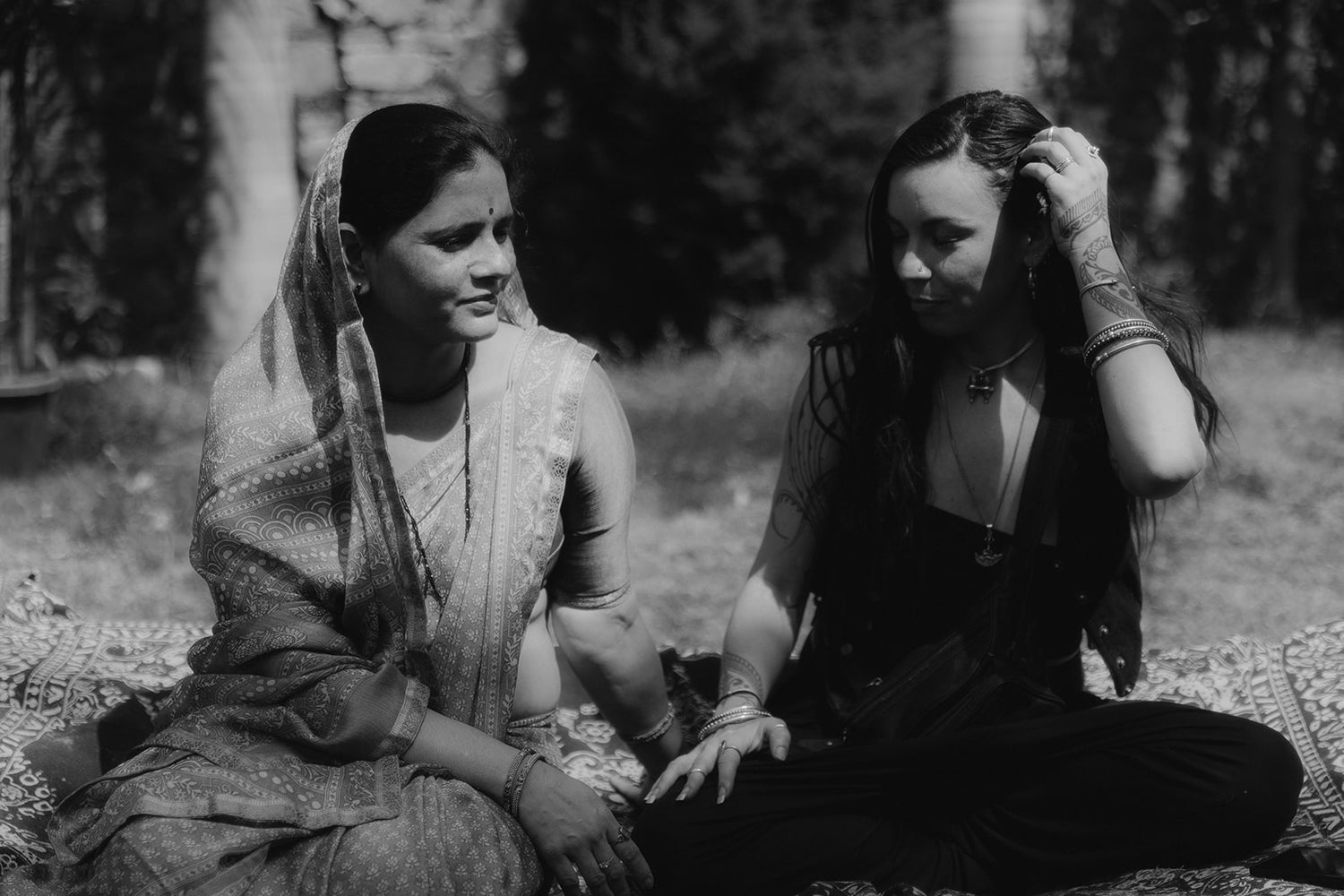 Two women from different cultures sitting together in quiet connection outdoors, symbolizing shared women's wisdom and cross-cultural understanding.