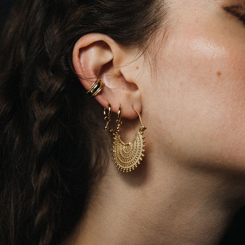 Woman wearing a layered ear stack with 925 sterling silver huggie earrings and gold vermeil hoops by Noir KĀLA.