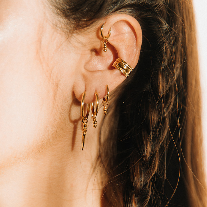Woman wearing a layered gold vermeil ear cuff earrings stack with hoops and spike charms by Noir KĀLA.