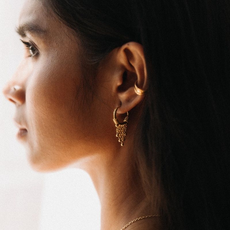 Woman wearing a 22K gold vermeil hoop earring with chain fringe and ear cuff showing proper gold vermeil care by Noir KĀLA.