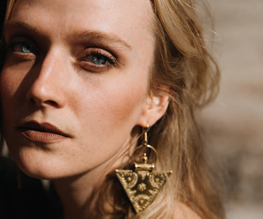 A woman wearing an engraved Noir KĀLA brass earring showing the amber-gold tone of solid nickel-free brass jewelry.