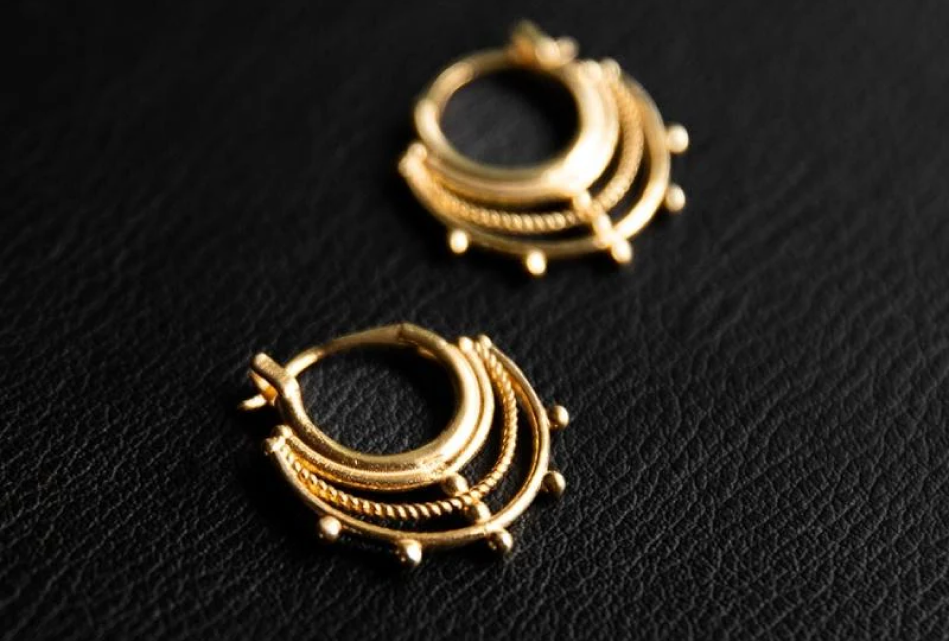 Granulation detail huggie hoop earrings in gold vermeil jewelry by Noir KĀLA on a black background.